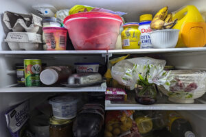 Interior of fridge stuffed with old food, produce, plastic bowls. 